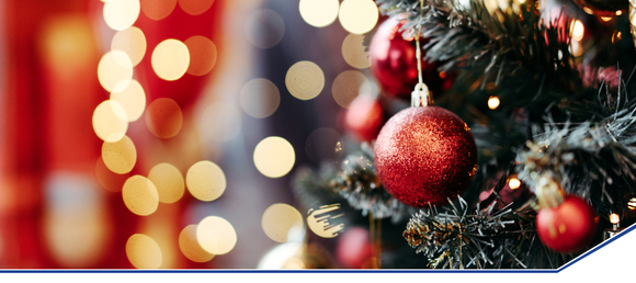 A festive Christmas tree adorned with red baubles and green branches, set against a soft, blurred background of warm yellow and red bokeh lights.
